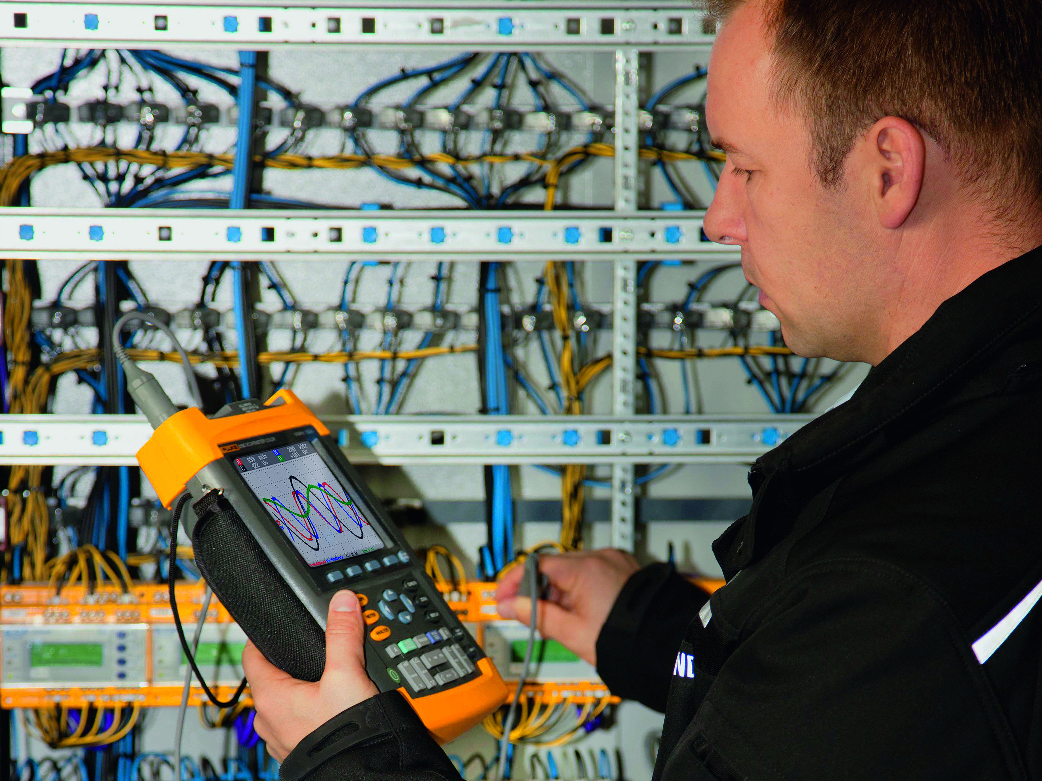 Techniker an Schaltschrank mit tragbarem Messgerät