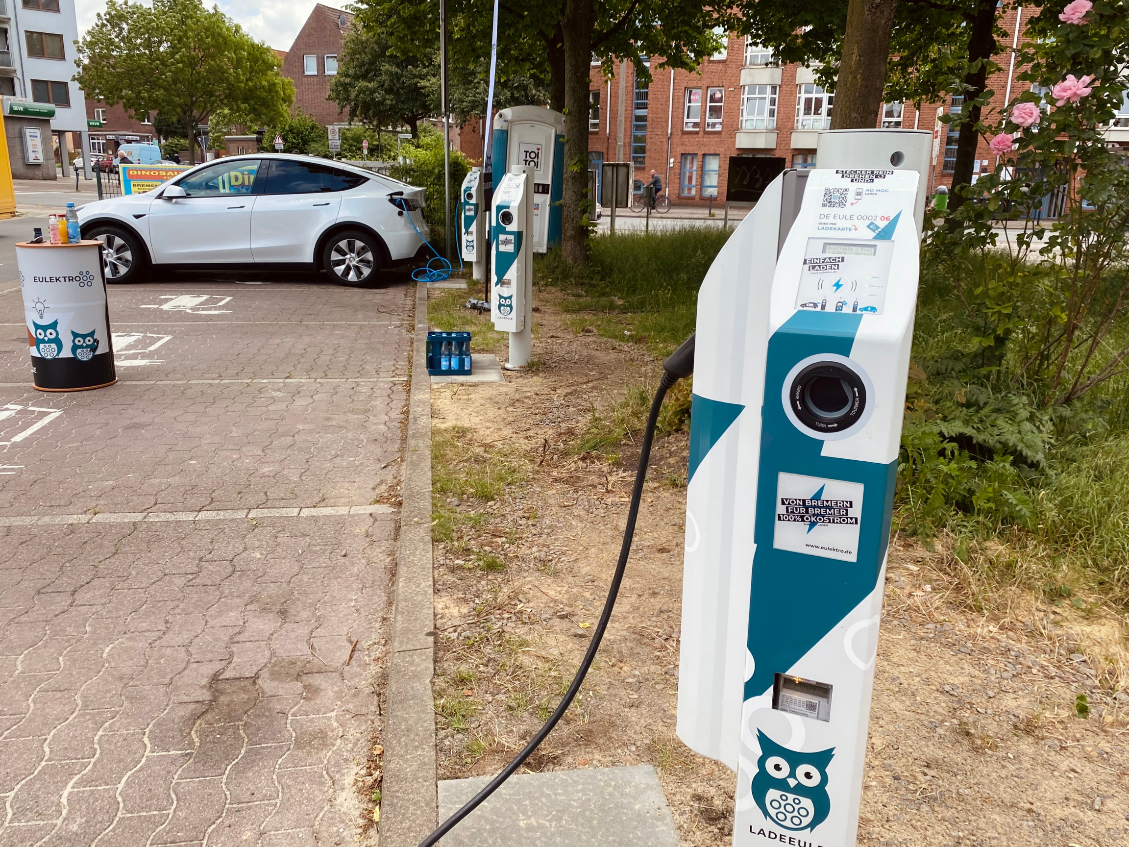 Ein weißes Elektroauto wird an einer Ladestation auf einem öffentlichen Parkplatz aufgeladen.