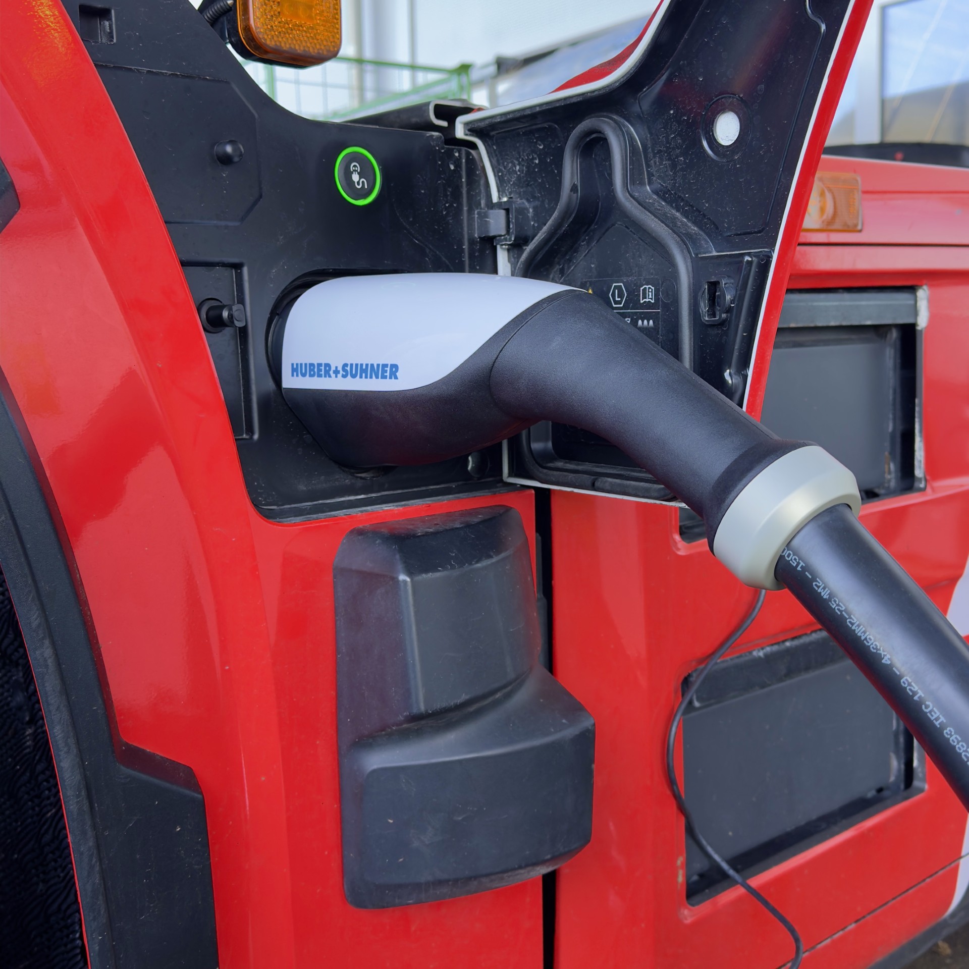 Ladestecker mit der Aufschrift 'HUBER+SUMNER' steckt in rotem Fahrzeug, Ladeanschlussklappe geöffnet.