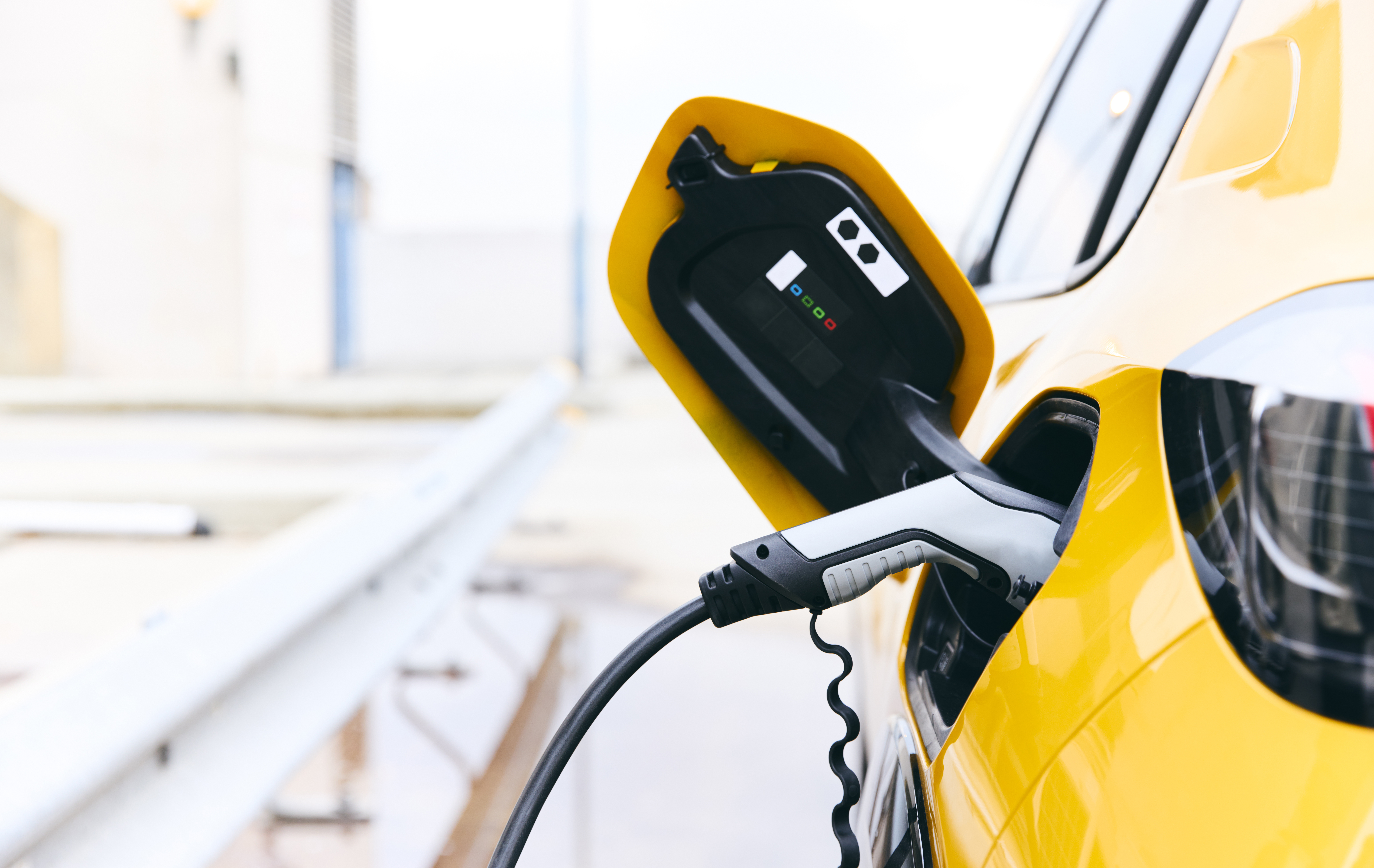 On voit une voiture électrique jaune branchée à une borne de recharge.